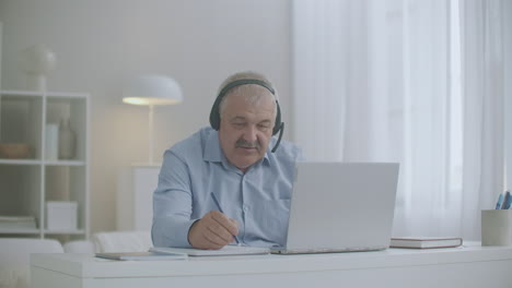 middle-aged-man-is-communicating-by-online-chat-with-colleagues-and-employees-from-home-using-laptop-and-headphones